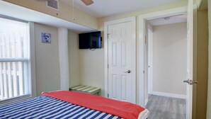 A bedroom with a bed, a television mounted on the wall, a door, and a window with blinds. - Nauti Mermaid Private Pool Sleeps 14 Dog Friendly (Port Aransas)