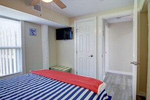Ein Schlafzimmer mit einem Bett, einem an der Wand montierten Fernseher, einer Tür und einem Fenster mit Jalousien.