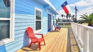 A blue building with a porch, red chairs, and a Texas flag. - Nauti Mermaid Private Pool Sleeps 14 Dog Friendly (Port Aransas)