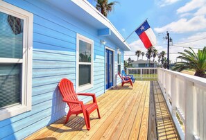 Ein blaues Gebäude mit einer Veranda, roten Stühlen und einer Texas-Flagge.