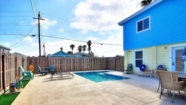 A backyard with a swimming pool, a wooden fence, and outdoor furniture. - Nauti Mermaid Private Pool Sleeps 14 Dog Friendly (Port Aransas)