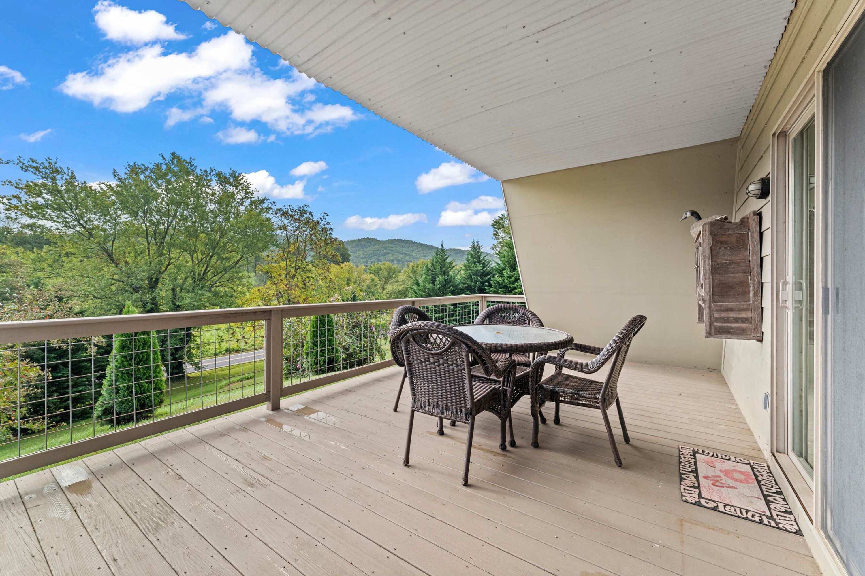 Un balcon abrité, doté de meubles en osier et offrant une vue sur un paysage verdoyant.