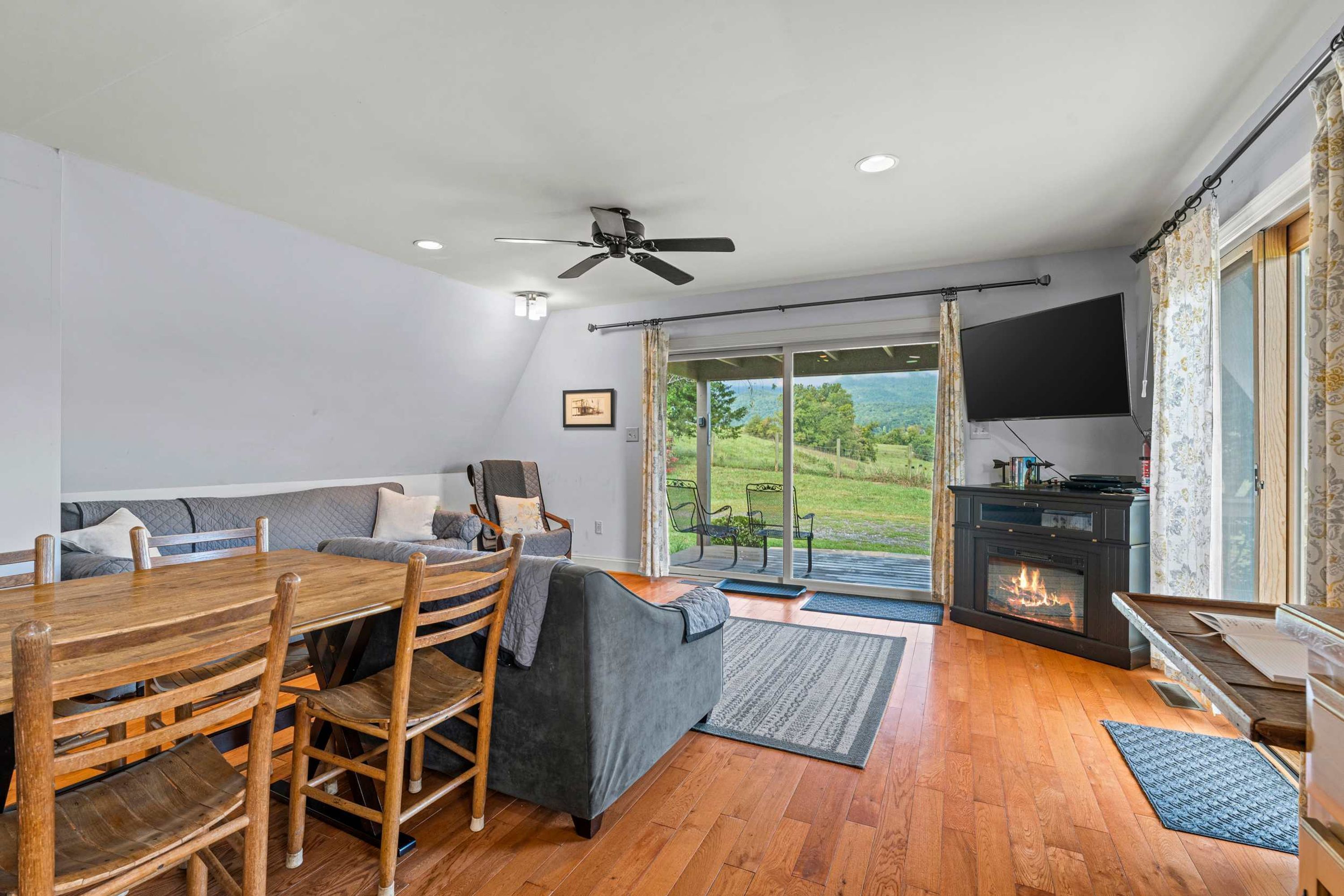 A modern living room with a wooden dining table, grey sofa, and a fireplace.