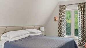 Quarto com cama, travesseiros, abajur e janela com cortinas.