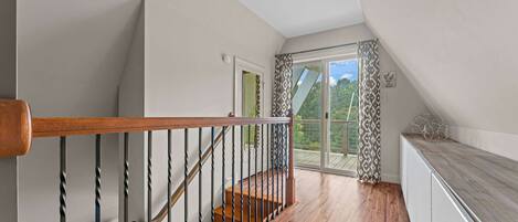 A staircase with a wooden handrail and black balusters leading to a landing with a glass door.