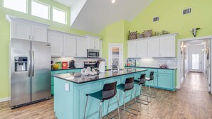 Una cocina moderna con armarios blancos, una isla central con taburetes y un microondas.