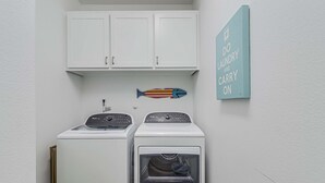 Un lavadero con dos lavadoras blancas, un adorno con forma de pez y un letrero que dice 'DO LAUNDRY AND CARRY ON'.