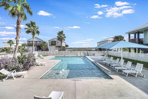 A swimming pool with lounge chairs and palm trees, surrounded by houses. - Brito Beach- View of Pond Propane Grill (Port Aransas)