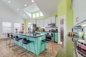 A modern kitchen with a central island, bar stools, and a dining area with a table and chairs. - Brito Beach- View of Pond Propane Grill (Port Aransas)