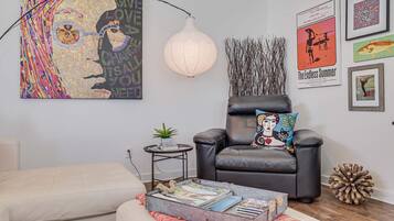 A living room with a sofa, a chair, a coffee table with books, a lamp, and wall art.
