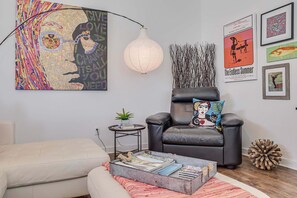 Una sala de estar con un sofá, una silla, una mesita de centro con libros, una lámpara y decoración en la pared.