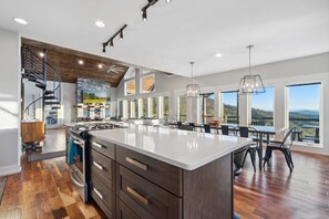 A modern kitchen with a large island, built-in appliances, and a dining area with a view. - 10min to Hatley Pointe Views Hottub Firepit (Mars Hill)