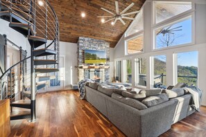 A spacious living area with a large gray sectional sofa, a fireplace, and a modern staircase. - 10min to Hatley Pointe Views Hottub Firepit (Mars Hill)