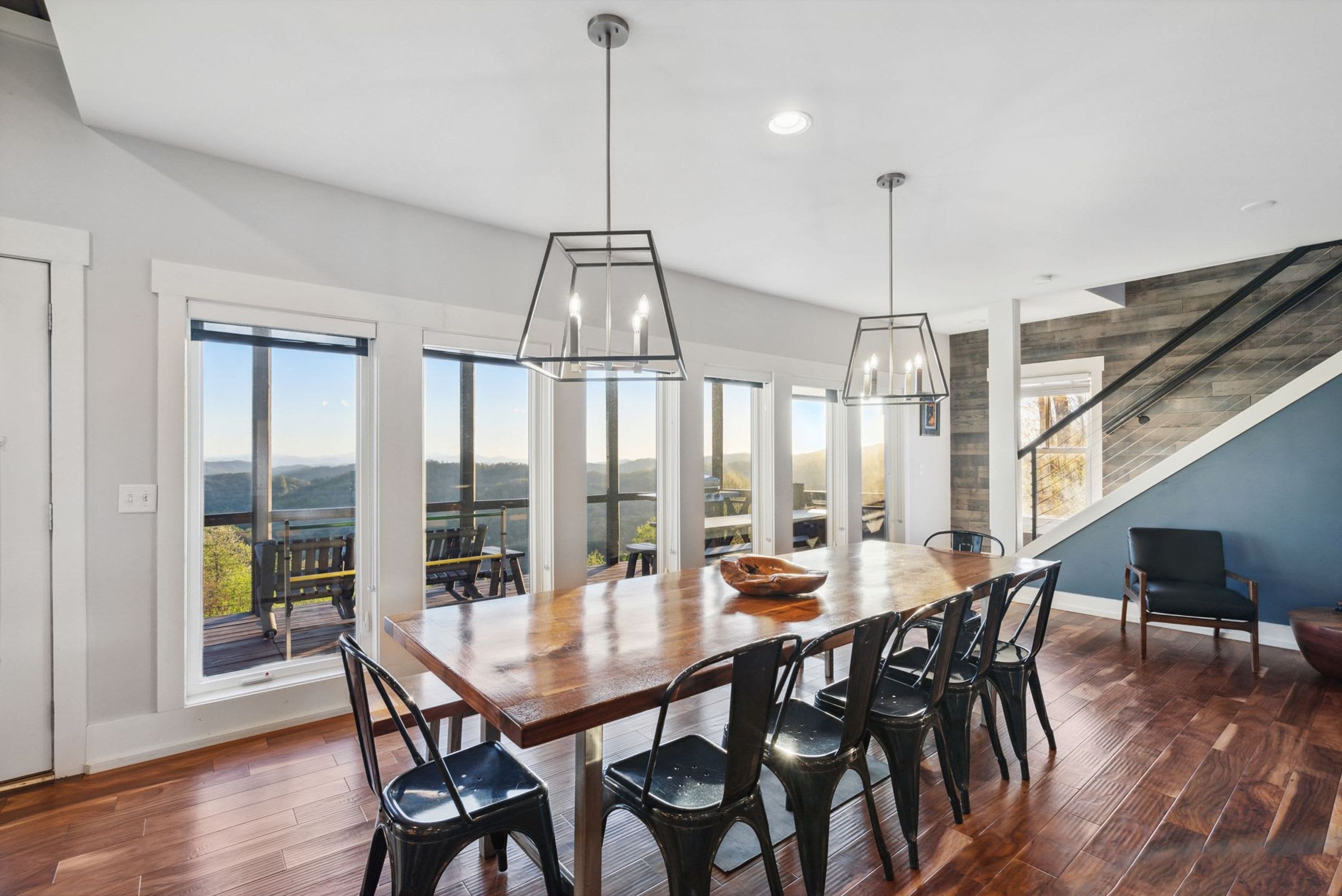 A spacious dining area with a large wooden table, black chairs, and pendant lighting.