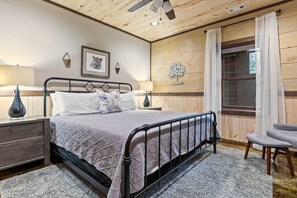 Ein Schlafzimmer mit einem Bett, Nachttischen, einem Sessel, einem Fenster mit Vorhängen und Wanddekoration.