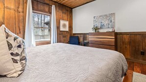 A bedroom with a large bed, wooden walls, a ceiling fan, a window with curtains, and a painting on the wall. - Blue Ridge Cabin Stunning Views Hot Tub Game Room (Cherry Log)