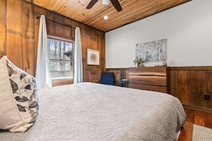 Ein Schlafzimmer mit einem großen Bett, Holzwänden, einem Deckenventilator, einem Fenster mit Vorhängen und einem Gemälde an der Wand.