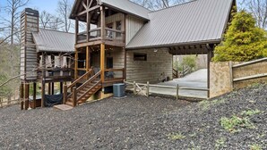 A two-story wooden cabin with a balcony, a covered porch, and a stone wall. - Blue Ridge Cabin Stunning Views Hot Tub Game Room (Cherry Log)