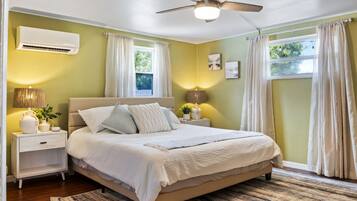 A bedroom with a bed, nightstands, an air conditioner, a ceiling fan, and curtains.