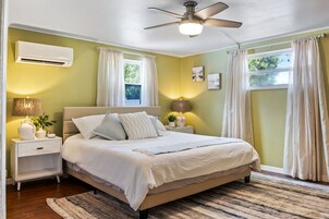 Un dormitorio con cama, mesitas de noche, aire acondicionado, ventilador de techo y cortinas.