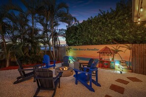 Un espacio al aire libre con sillas, un brasero, un bar tiki y un mural de una playa.