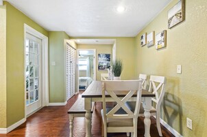 Un comedor con mesa y sillas, vista al exterior y puerta que da a otra habitación.