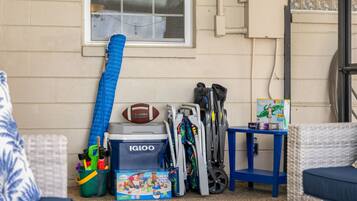 A room with a window, a blue chair, a wicker sofa, a blue table, and various children's toys and equipment.