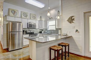 Una cocina con gabinetes blancos, electrodomésticos de acero inoxidable, encimera de granito y una isla grande con taburetes.