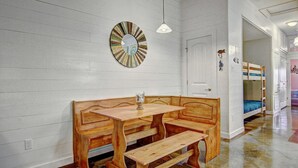 A room with a wooden bench and table, a wall clock, and bunk beds in the background. - Gone Coastal Private Breezeway Family Friendly (Port Aransas)
