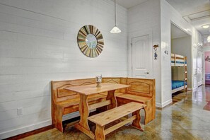 A room with a wooden bench and table, a wall clock, and bunk beds in the background. - Gone Coastal Private Breezeway Family Friendly (Port Aransas)