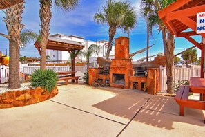 An outdoor patio area with a stone fire pit, wooden benches, and palm trees. - Gone Coastal Private Breezeway Family Friendly (Port Aransas)