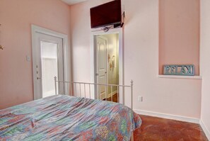 A bedroom with a bed, a door, a television mounted on the wall, and a small shelf with a nameplate. - Gone Coastal Private Breezeway Family Friendly (Port Aransas)