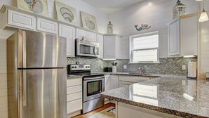 A kitchen with white cabinets, stainless steel appliances, a granite countertop, and decorative wall art. - Gone Coastal Private Breezeway Family Friendly (Port Aransas)