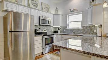 A kitchen with white cabinets, stainless steel appliances, a granite countertop, and decorative wall art.