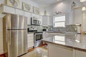 A kitchen with white cabinets, stainless steel appliances, a granite countertop, and decorative wall art. - Gone Coastal Private Breezeway Family Friendly (Port Aransas)