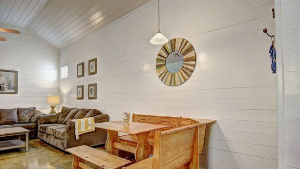 A cozy room with a wooden dining table and benches, a sofa, and a wall-mounted round mirror. - Gone Coastal Private Breezeway Family Friendly (Port Aransas)