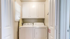 A laundry room with two washers and dryers, white cabinets above, and a fire exit sign on the door. - Casa Bella- Community Pool View 0 3 mi to Beach (Port Aransas)