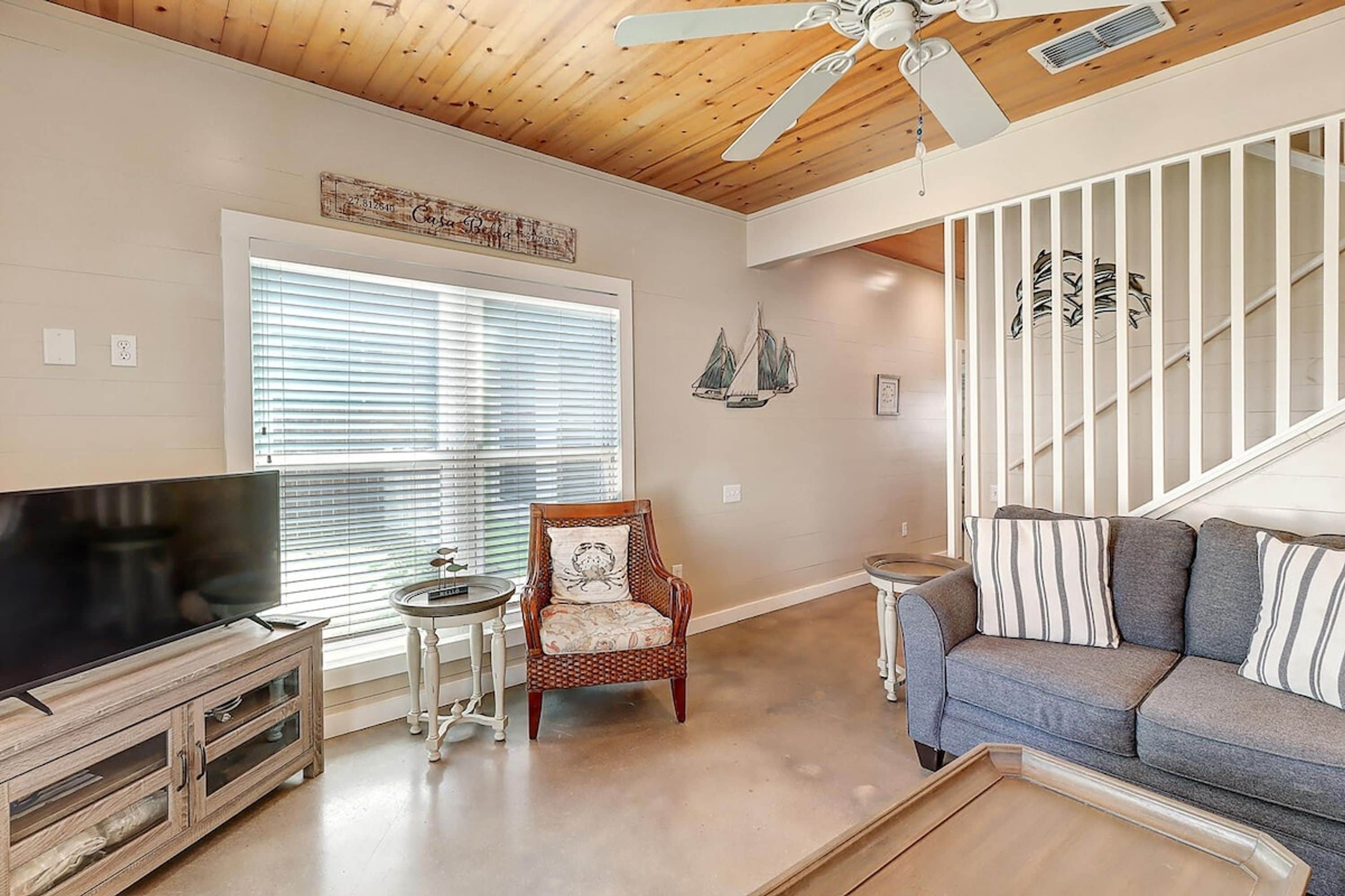 A living room with a wooden ceiling, a television, a sofa, a chair, and a staircase with a railing.