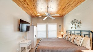 A bedroom with a bed, a TV mounted on the wall, a ceiling fan, and a window with blinds. - Casa Bella- Community Pool View 0 3 mi to Beach (Port Aransas)