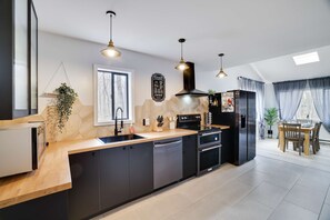A modern kitchen with a central island, black cabinetry, and pendant lighting. - 3BR Home w Outdoor Fun Lake Fire Pit Games Grill (Tobyhanna)
