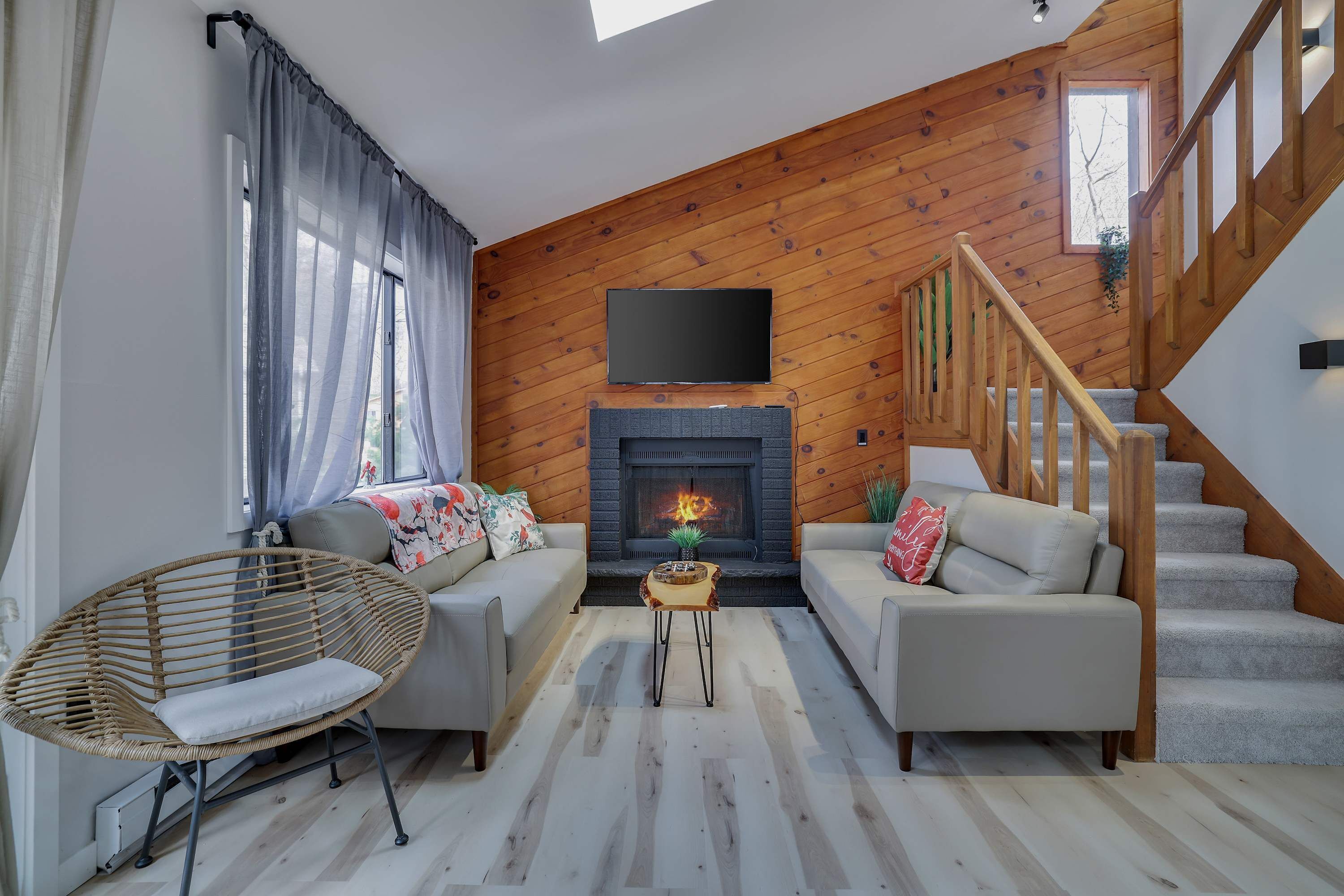 A living room with a fireplace, two sofas, a wicker chair, a small table, and a staircase.
