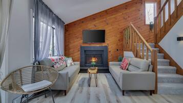 A living room with a fireplace, two sofas, a wicker chair, a small table, and a staircase.