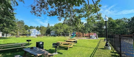 A park with picnic tables, a playground, and a lamp post.