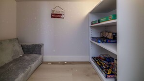 Una habitación con un sofá, un cartel en la pared que dice 'WIZARDS welcome' y una estantería llena de juegos de mesa.