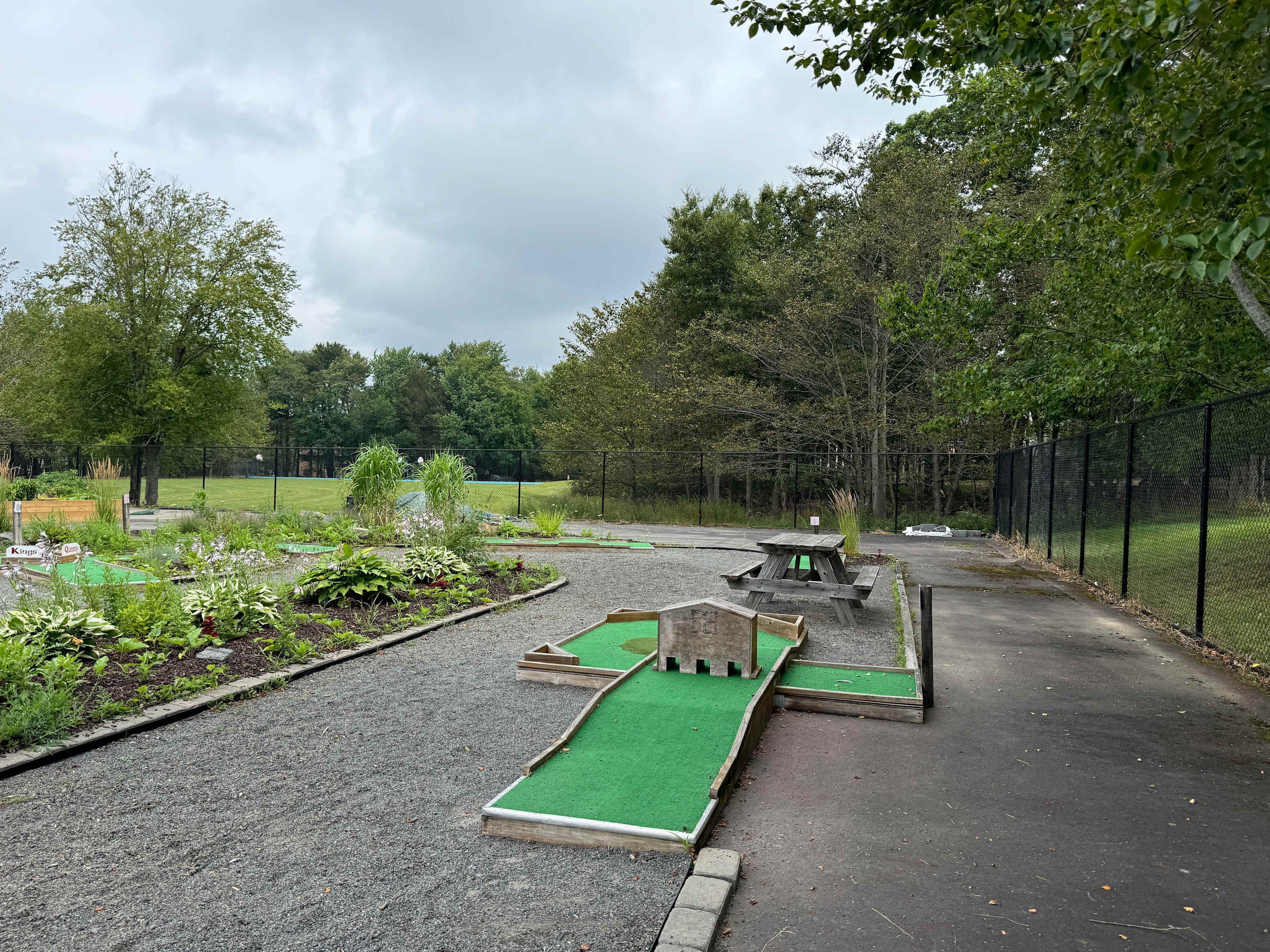 Un parcours de mini-golf avec des tapis de putting verts, des obstacles en bois et une table de pique-nique.