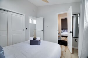 Quarto com cama, um cesto de armazenamento, porta e vista para outro espaço.