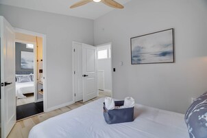Habitación de hotel con cama, ventilador de techo, un cuadro y un baño visible a través de una puerta abierta.