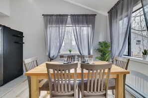 Un coin repas avec une table et des chaises en bois, un réfrigérateur noir et une fenêtre ornée de rideaux légers.