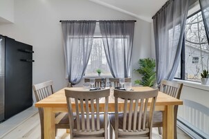 A dining area with a wooden table and chairs, a black refrigerator, and a window with sheer curtains.