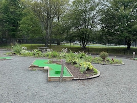 Un espacio al aire libre con camas elevadas para jardín, una mesa de picnic y un campo deportivo cercado.